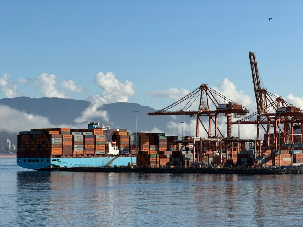 Container ship docked at Vancouver's bustling port with cranes and mountains in view.